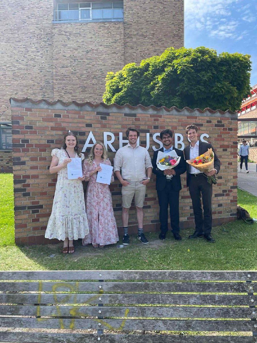 Jesper N. Wulff with graduating students holding theses and flowers in front of the Aarhus BSS sign