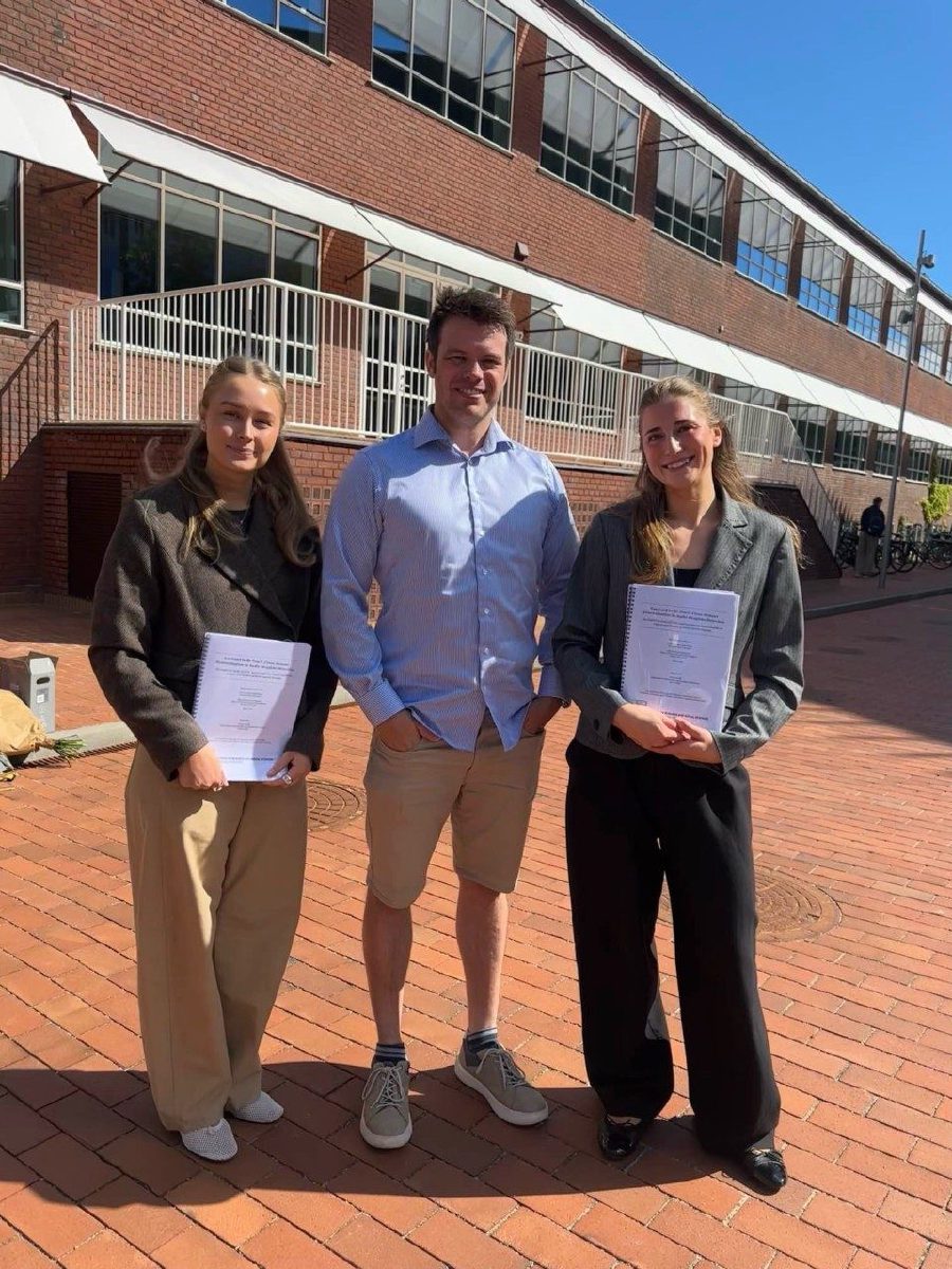 Jesper N. Wulff with two master's thesis students holding their bound theses outside Aarhus BSS